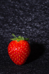 FIRST PLANE OF STRAWBERRY PROJECTING ITS SHADOW ISOLATED IN BACKGROUND WITH BLACK TEXTURES