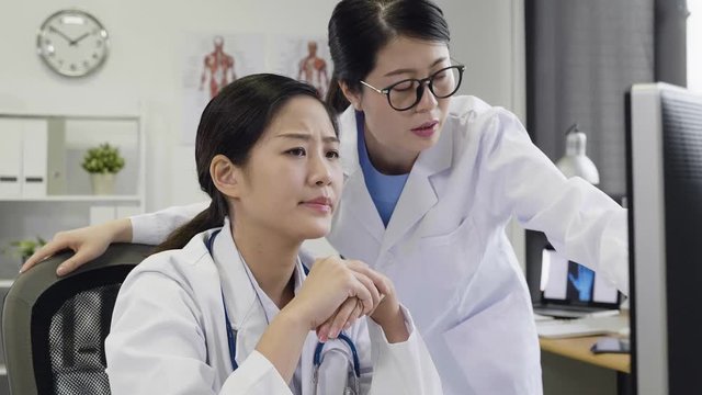 slow motion of asian medical team discussing around computer in hospital office. Two doctors talking about patient situation on screen monitor. young female healthcare worker working together consult