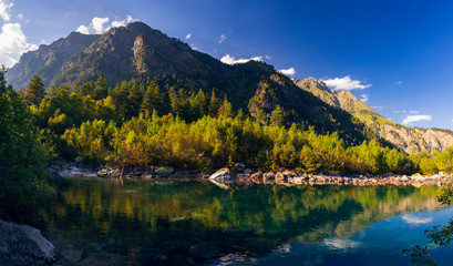 A huge panorama of the High-mountainous Baduk lake among the high Caucasian mountains and beautiful trees. Sunny summer day.