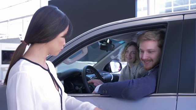 Auto business, saleswoman advise clients young couple sitting in car salon while buying new family vehicle at auto show
