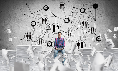 Attractive man sitting on pile of paper documents.