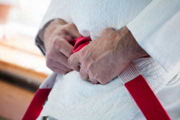 Hands of an elderly coach with a red-white judo belt and kimono.