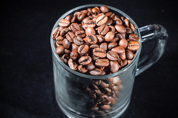 Glass cup of coffee with coffee beans on a dark background, close-up, in a low key