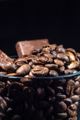 Glass cup of coffee with coffee beans and chocolate on a dark background, close-up in a low key