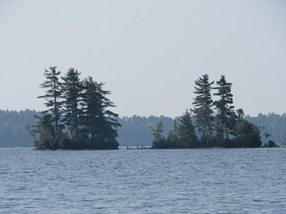 View across Damariscotta Lake in Maine on a cloudy day of two islands with stacked stones, or cairns, in between them