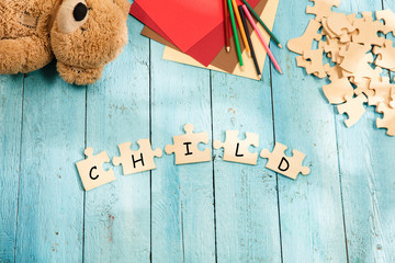 Stationery and word CHILD made of letters, mock up and pieces of puzzles on wooden background. Concept of family, baby, pregnancy, maternity, parenting, children.