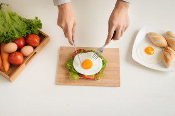 Hands of man cut the eggs on cutting board, served with bread, herbs, sausage and fresh juice.