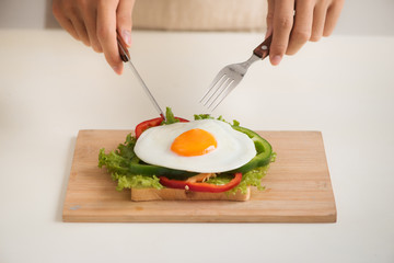 Hands of man cut the eggs on cutting board, served with bread, herbs, sausage and fresh juice.