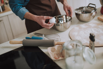 Hand holding one egg near the metal bowl