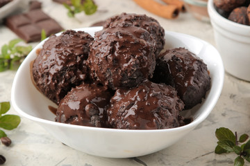 Chocolate ice cream with liquid chocolate on a light concrete background.