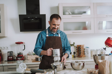 Bearded man looking at the flour while sifting it and smiling