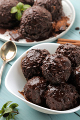Chocolate ice cream with liquid chocolate and with a cinnamon stick, coffee beans and almonds on a blue wooden background.