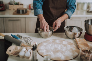 Man kneading dough in the bowl while standing in the kitchen