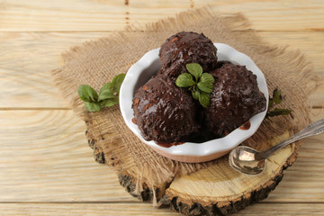 Chocolate ice cream with liquid chocolate and a mint leaf on a natural wooden background.