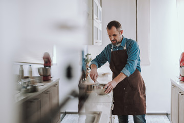 Concentrated bearded man whisking eggs on the countertop