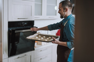 Smiling man holding sheet pan and opening the oven