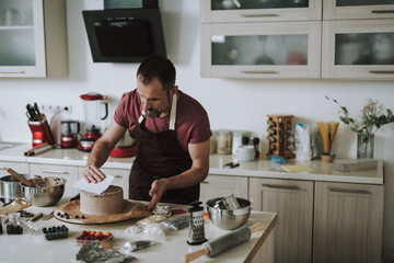 Careful bearded man using cake scraper while cooking