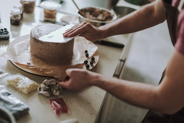 Hands of professional confectioner smoothing the cake