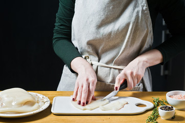 The chef cuts raw squid into rings on the cutting Board. Black background, side view, kitchen