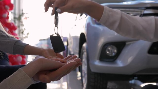 family car purchase, auto dealer gives keys new automobile to owners hands parents with small child close-up against of machine in sales center