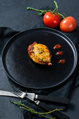 Baked squid in tomato sauce on a black plate. Black background, side view