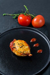 Baked squid in tomato sauce on a black plate. Black background, side view