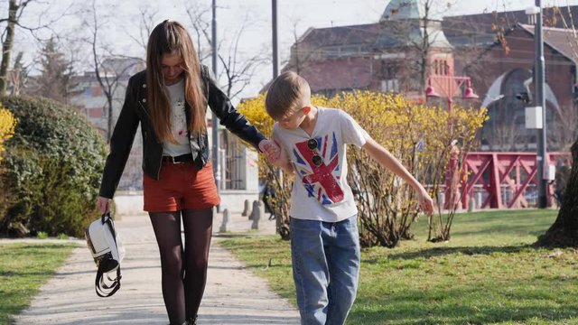 Teenage friends kid boy teaches his girlfriend to ride skateboard in a park