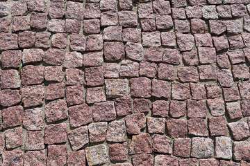 Paving stone laid out of square granite stones of brown color. Stones with jagged edges. The texture of the stones is mottled with dark dots. Day, the pavement lit by sunlight. Background, backdrop.