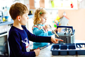 Cute little toddler girl and school boy helping in the kitchen with dish washing machine. Happy...