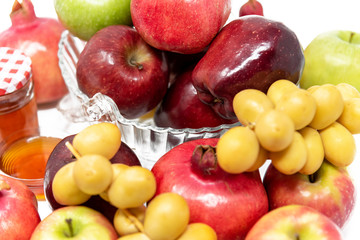 Rosh Hashanah (Jewish New Year) Traditional Symbols, Honey in a glass jar, Pomegranates, Dates, Red And Green Apples. Isolated On A White Background