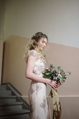 Young woman posing in a light long lace dress with a bouquet of flowers in her hands