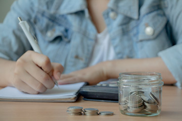 Fototapeta na wymiar money in glass jar with calculator and female hand writing on note pad 