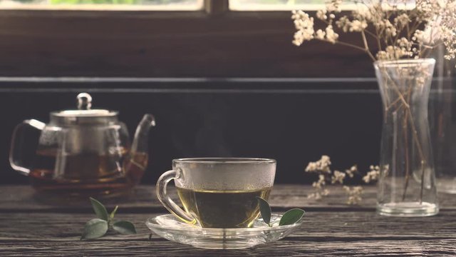 Hot organic tea in glass cup with steam on wooden table with view of room on the morning, Vintage style