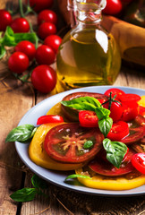 Salad of colorful tomatoes on plate with ingredients. Vintage wooden kithen table background, selective focus
