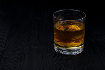 A glass of whisky with ice on the ebony table.