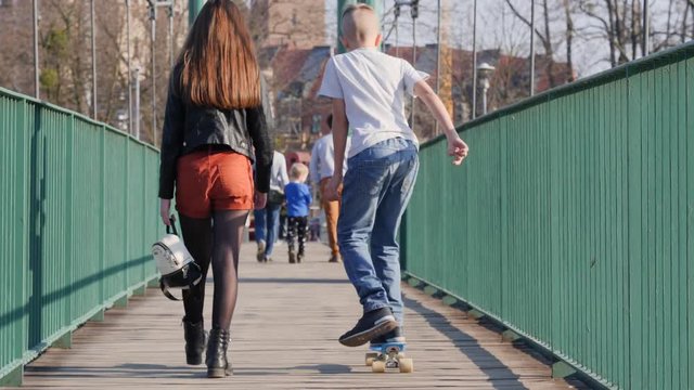 Teenage friends boy and girl kids walking together with skateboard over the bridge in a city daytime