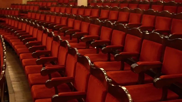 Soft red velor or velvet chairs in the opera house. Rows of empty spectator seats before the start of the performance. Point of view, the first perspective of the viewer, who goes to his place.