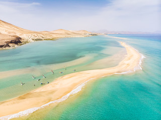 Luftaufnahme des Strandes auf der Insel Fuerteventura mit Windsurfern, die während der Sommerferien in türkisblauem Wasser Windsurfen lernen, Kanarische Inseln von Drohne