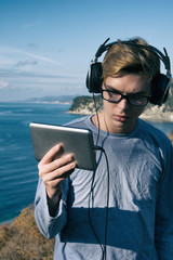 Cold weather. Young attractive guy is resting on the sea and listening to music.