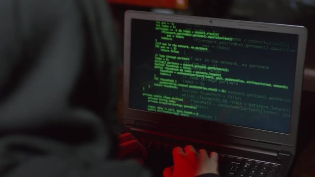 Back view of hooded hacker sitting in caf&eacute; at laptop and coding