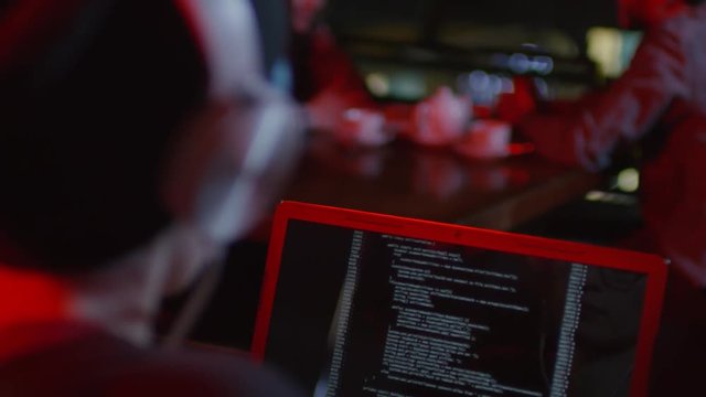 Rare view of young male software developer sitting at laptop in bar and coding while people on background having meal