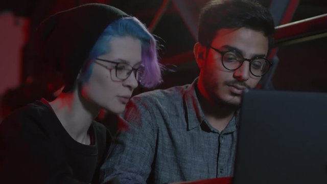 Medium shot of two male and female hackers sitting at laptop and coding