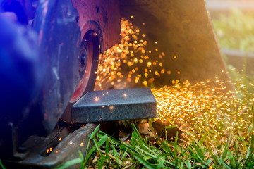 worker cutting metal with grinder at outdoor lawn or construction site