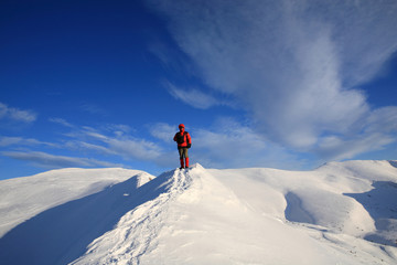Fototapeta na wymiar The tourist stands on the ridge of the mountains in the winter mountains
