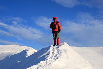 Naklejka na ściany i meble The tourist stands on the ridge of the mountains in the winter mountains