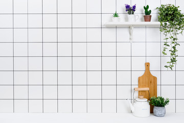 Various kinds of kitchen tools arranged on the white table. And tidy flower pots are placed neatly on the shelf.