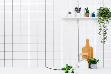 Various kinds of kitchen tools arranged on the white table. And tidy flower pots are placed neatly on the shelf.