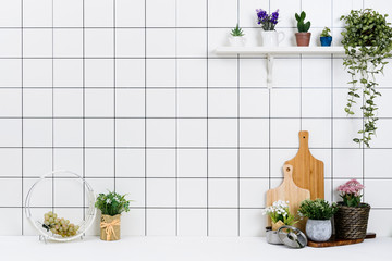 Various kinds of kitchen tools arranged on the white table. And tidy flower pots are placed neatly on the shelf.