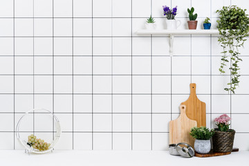 Various kinds of kitchen tools arranged on the white table. And tidy flower pots are placed neatly on the shelf.