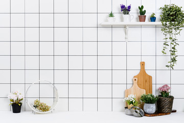 Various kinds of kitchen tools arranged on the white table. And tidy flower pots are placed neatly on the shelf.